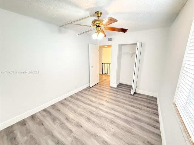 unfurnished bedroom featuring a textured ceiling, visible vents, a closet, and light wood-type flooring