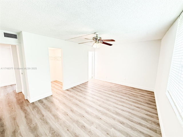 spare room with light wood-type flooring, visible vents, a textured ceiling, and a ceiling fan