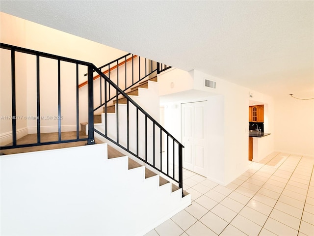 stairway with tile patterned floors, visible vents, and a textured ceiling