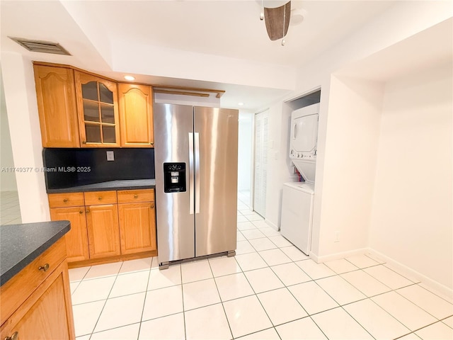 kitchen with visible vents, glass insert cabinets, stacked washer / drying machine, stainless steel refrigerator with ice dispenser, and dark countertops