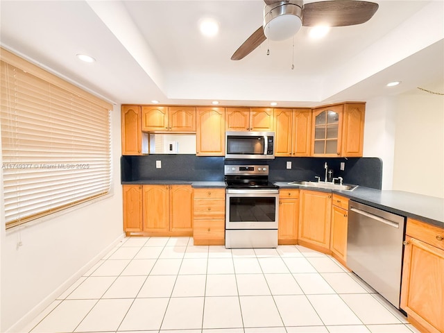 kitchen with a sink, a tray ceiling, tasteful backsplash, appliances with stainless steel finishes, and glass insert cabinets