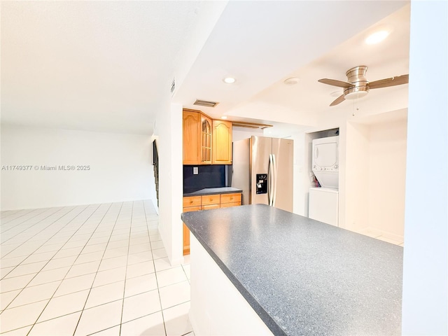 kitchen featuring visible vents, stainless steel refrigerator with ice dispenser, dark countertops, recessed lighting, and stacked washer / drying machine