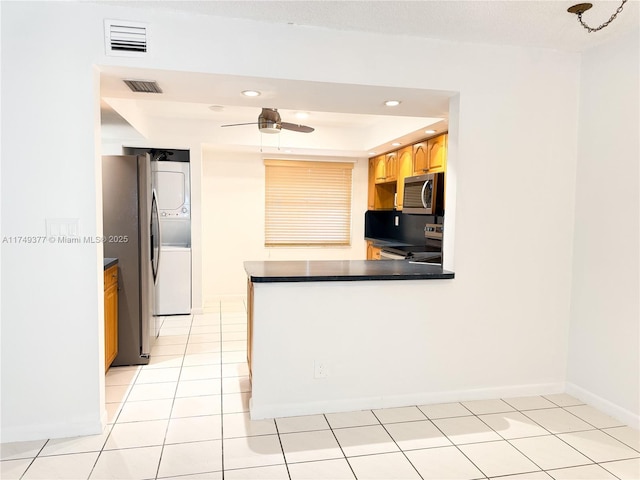 kitchen featuring visible vents, dark countertops, stacked washing maching and dryer, appliances with stainless steel finishes, and light tile patterned flooring