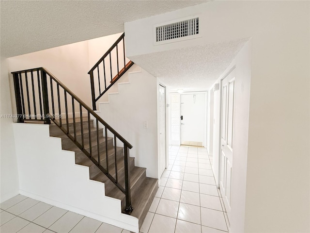 stairs with tile patterned floors, visible vents, and a textured ceiling