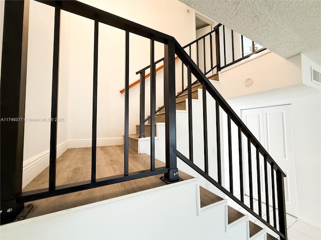 staircase featuring visible vents, a textured ceiling, and wood finished floors