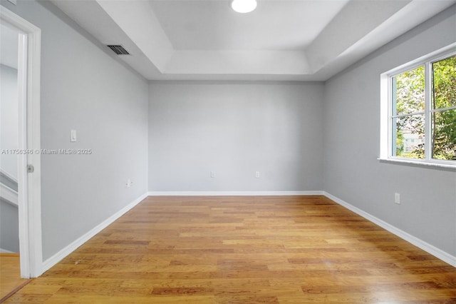 spare room with a raised ceiling, visible vents, light wood-style flooring, and baseboards