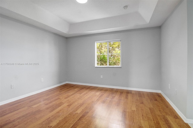 unfurnished room featuring light wood-style flooring, baseboards, and a tray ceiling