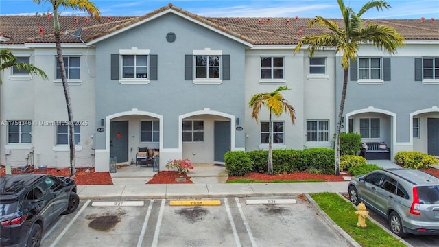 townhome / multi-family property with stucco siding, uncovered parking, and a tiled roof