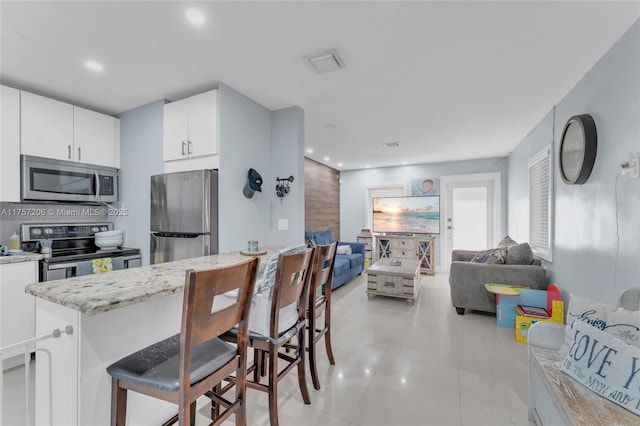 kitchen with visible vents, white cabinets, a breakfast bar area, light stone countertops, and stainless steel appliances