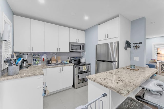 kitchen with a sink, white cabinetry, appliances with stainless steel finishes, backsplash, and a kitchen bar