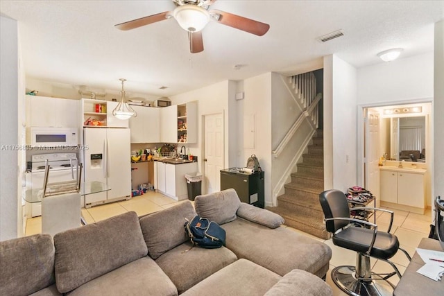 living area featuring light tile patterned floors, ceiling fan, stairway, and visible vents