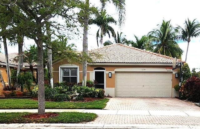 view of front of house featuring a tiled roof, decorative driveway, an attached garage, and stucco siding