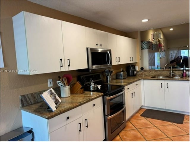 kitchen featuring appliances with stainless steel finishes, dark stone countertops, white cabinetry, a sink, and light tile patterned floors