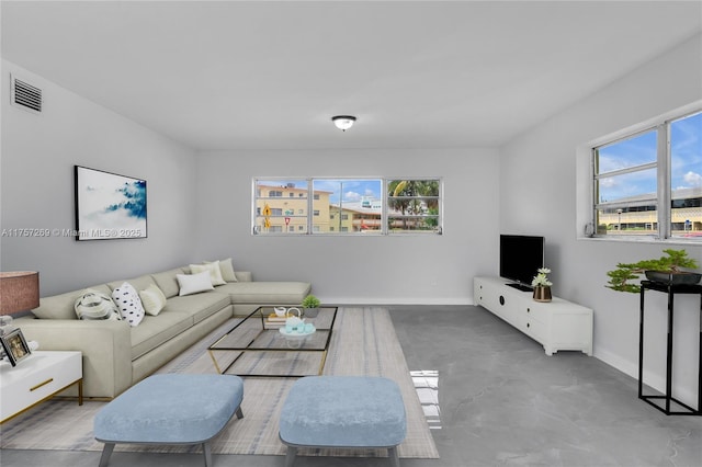 living area featuring concrete flooring, a healthy amount of sunlight, visible vents, and baseboards