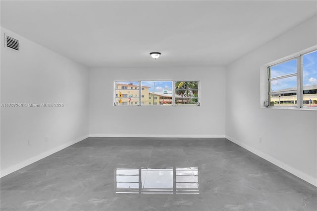 spare room featuring concrete flooring, a healthy amount of sunlight, visible vents, and baseboards