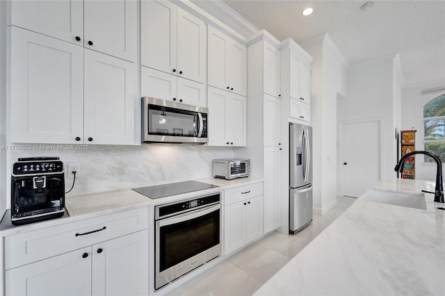 kitchen featuring a toaster, decorative backsplash, appliances with stainless steel finishes, white cabinets, and a sink