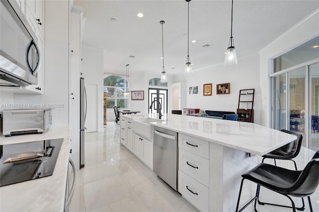 kitchen with white cabinets, a large island, appliances with stainless steel finishes, pendant lighting, and a sink