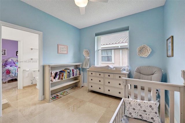 bedroom with a nursery area, ceiling fan, a textured ceiling, and baseboards