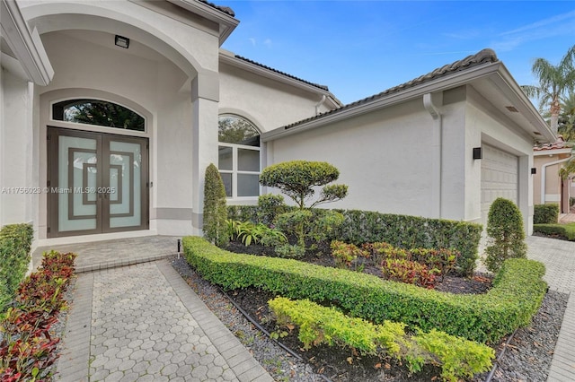 view of exterior entry with an attached garage, decorative driveway, french doors, and stucco siding