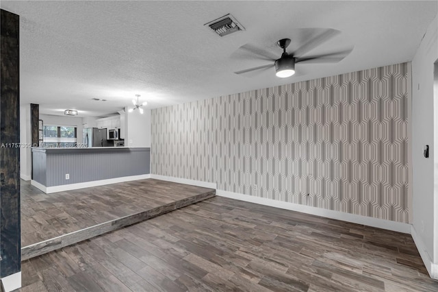 unfurnished room featuring visible vents, ceiling fan, a textured ceiling, wood finished floors, and baseboards