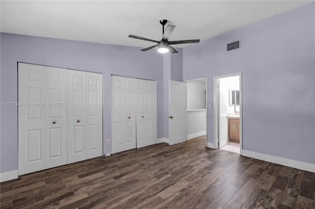 unfurnished bedroom featuring dark wood-style flooring, visible vents, baseboards, vaulted ceiling, and two closets