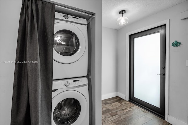 laundry room featuring stacked washer and clothes dryer, a textured ceiling, wood finished floors, laundry area, and baseboards