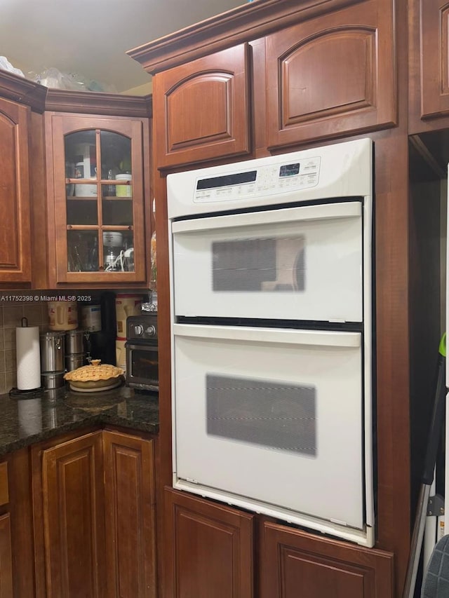 kitchen featuring glass insert cabinets, dark stone counters, and white double oven