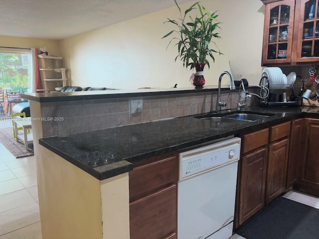 kitchen with tasteful backsplash, glass insert cabinets, white dishwasher, a sink, and light tile patterned flooring