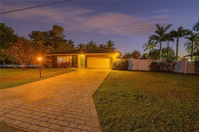 view of front of house featuring an attached garage, fence, decorative driveway, a front lawn, and stucco siding