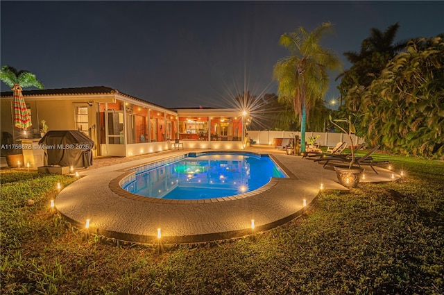 pool at night featuring a patio area, a fenced in pool, a fenced backyard, and a sunroom