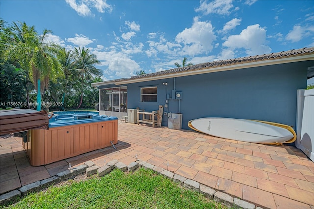 back of house featuring stucco siding, a hot tub, a sunroom, a patio area, and a tiled roof