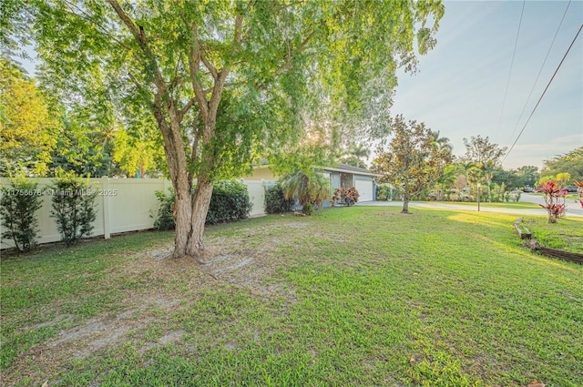 view of yard with a garage, fence, and driveway