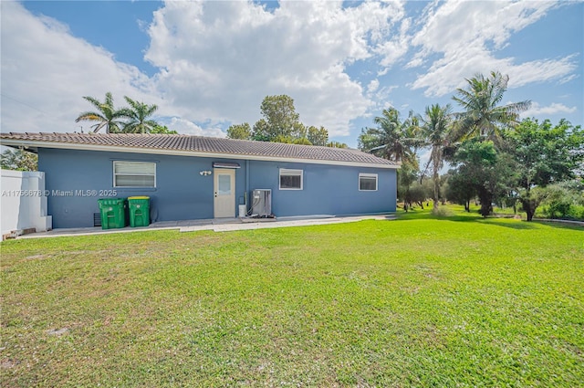 rear view of house with a lawn, a tiled roof, fence, a patio area, and stucco siding