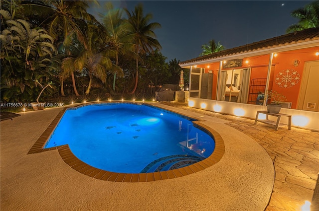 pool at night featuring a patio area