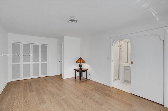 unfurnished bedroom with baseboards, visible vents, arched walkways, connected bathroom, and light wood-style floors