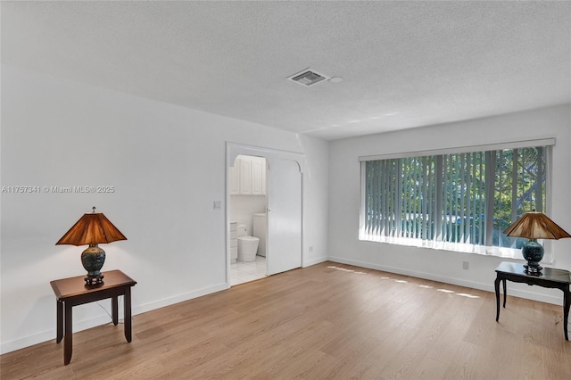 interior space featuring visible vents, a textured ceiling, baseboards, and wood finished floors