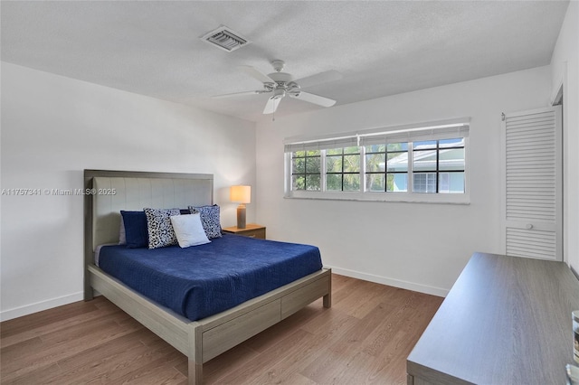 bedroom with visible vents, a ceiling fan, a textured ceiling, wood finished floors, and baseboards