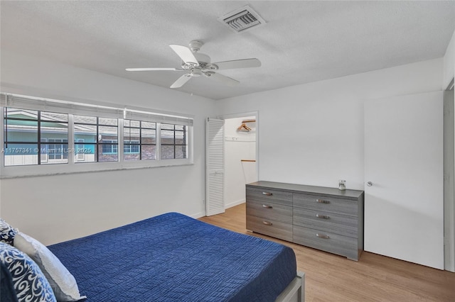 bedroom featuring light wood finished floors, ceiling fan, visible vents, and a textured ceiling