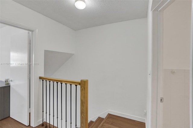 corridor featuring a textured ceiling, wood finished floors, and an upstairs landing