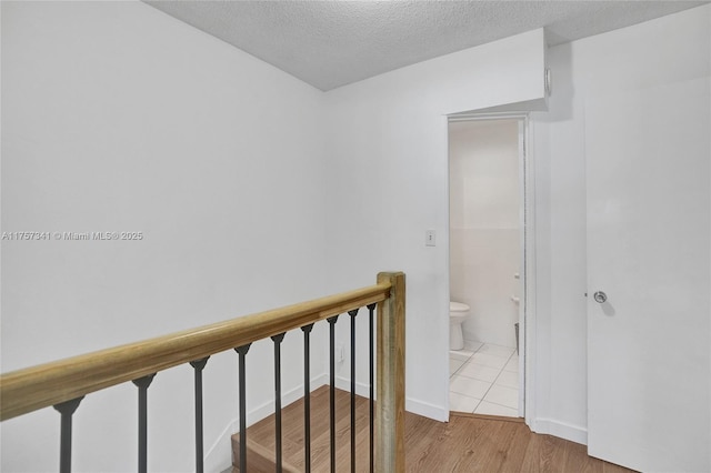 hallway featuring a textured ceiling, wood finished floors, an upstairs landing, and baseboards