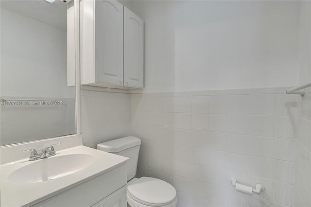 bathroom featuring toilet, wainscoting, tile walls, and vanity