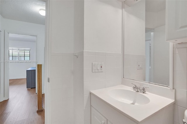 bathroom with a textured ceiling, toilet, wood finished floors, vanity, and tile walls