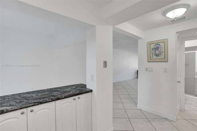 kitchen with light tile patterned floors, visible vents, white cabinets, dark stone counters, and baseboards