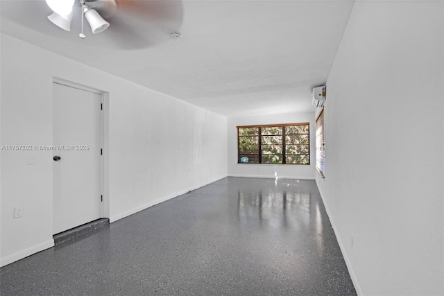 spare room featuring a ceiling fan, a wall unit AC, baseboards, and speckled floor