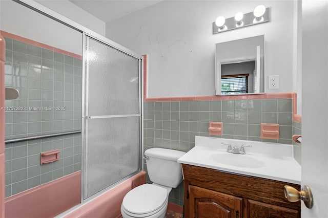 bathroom with toilet, a wainscoted wall, enclosed tub / shower combo, vanity, and tile walls