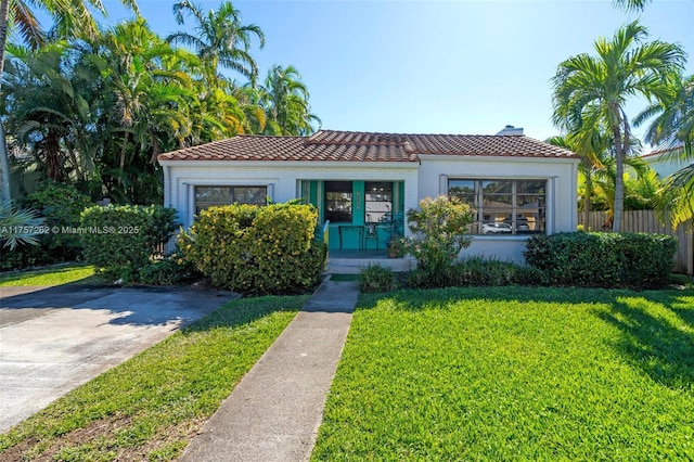 mediterranean / spanish home with brick siding, a chimney, a front yard, fence, and a tiled roof