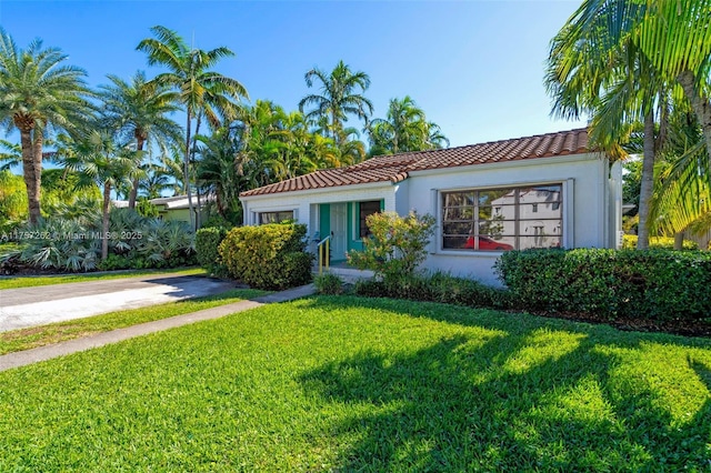 mediterranean / spanish-style home featuring a tile roof, driveway, a front lawn, and stucco siding