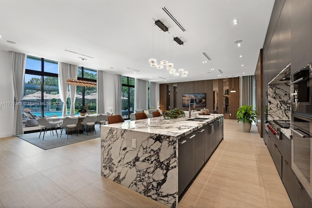 kitchen featuring light stone counters, decorative light fixtures, stainless steel oven, modern cabinets, and a large island with sink