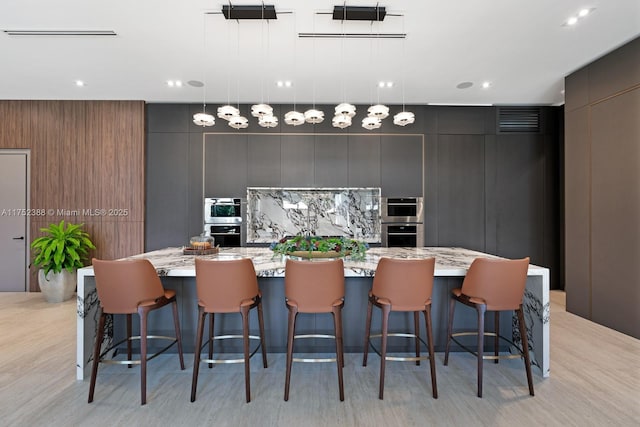 kitchen with a spacious island, modern cabinets, light stone counters, and decorative light fixtures