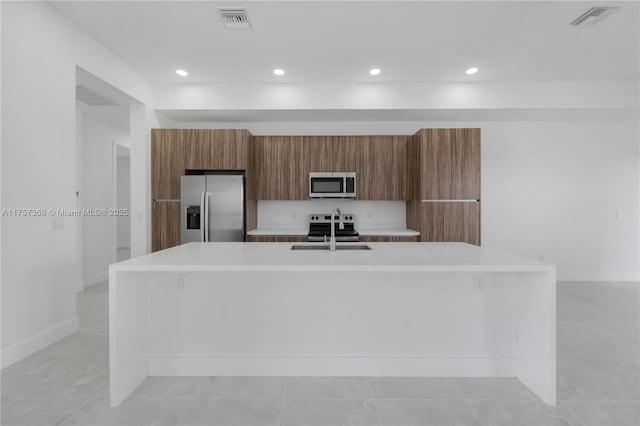 kitchen with a sink, visible vents, light countertops, appliances with stainless steel finishes, and brown cabinetry